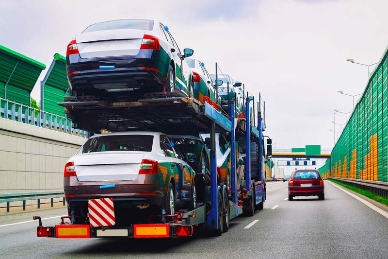 Ein Autotransport-Lkw transportiert mehrere Fahrzeuge auf der Autobahn, während grüne Lärmschutzwände den Straßenrand säumen.