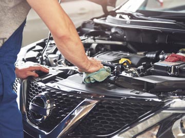 Ein Mechaniker wischt den Motor eines Nissan-Autos ab und konzentriert sich auf die Wartung in einer gut beleuchteten Garage.